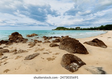 Beach with smooth, golden sand and smooth rocks scattered along the shore with cloudy sky - Powered by Shutterstock