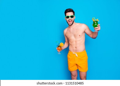 Beach style! Attractive and cheerful man in yellow shorts and eyeglasses, holds cocktails with small umbrella in hands, isolated on blue background. Concept of joyful hot summer - Powered by Shutterstock