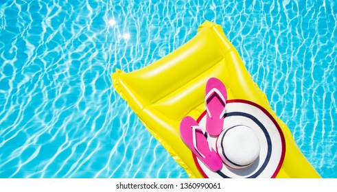 Beach summer holiday background. Inflatable air mattress, flip flops and hat on swimming pool. Yellow lilo and summertime accessories on poolside. Top view and copy space. Banner