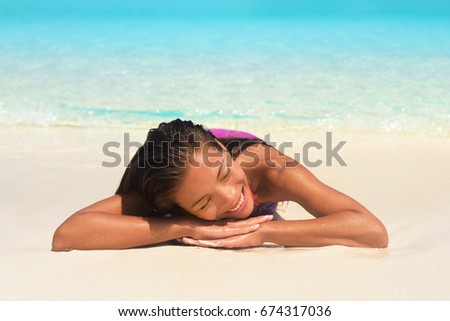 Beach summer relaxation spa retreat woman sunbathing lying down on white sand in tropical paradise. Bikini Asian girl relaxing sleeping enjoying sun getaway.