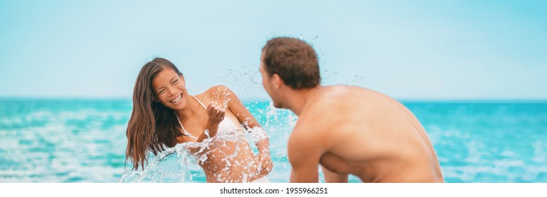 Beach Summer Vacation Happy Couple Having Fun Playing In Ocean Swimming Suit Splashing Water At Each Other Panoramic Banner. Asian Bikini Woman, Man.