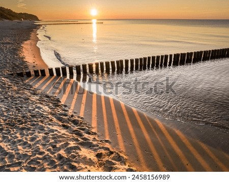 Beach and sun rays through breakwater at sunrise by Sea, Poland