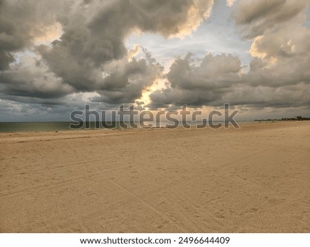beach sunset with large clouds and still water, sun behind clouds