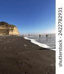 Beach sunset with a rock mountain landsscape, dark sand and small volcanic stones with people talking and watching the sea and the immense blue sky.