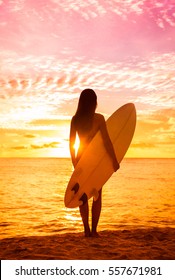 Beach sunset sexy surfer woman surfing lifestyle relaxing holding surfboard looking at ocean waves for surf. Active healthy living silhouette of sports athlete standing in colorful sky.