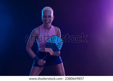 Beach tennis player woman with racket on tournament. Girl athlete with beach tenis racket on court with neon colors. Sport concept. Photo for design of a sports app or tour events.