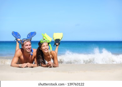 Beach travel couple having fun snorkeling. Happy young multiracial couple lying on summer beach sand with snorkel equipment looking to side at copy space after swimming with fins and mask on vacation. - Powered by Shutterstock