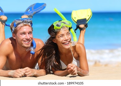 Beach travel couple having fun snorkeling. Happy young multiracial couple lying on summer beach sand with snorkel equipment looking to side at copy space after swimming with fins and mask on vacation. - Powered by Shutterstock