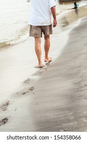 Beach Travel - Man Walking On Sand Beach Leaving Footprints In The Sand. Closeup Detail Of Male Feet