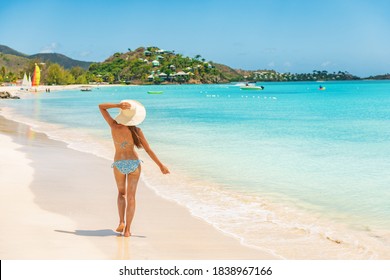 Beach travel vacation woman walking on luxury Caribbean cruise destination Antigua island in bikini wearing beach hat, carefree on holidays on Jolly Beach. Girl on travel vacation holidays swim model.