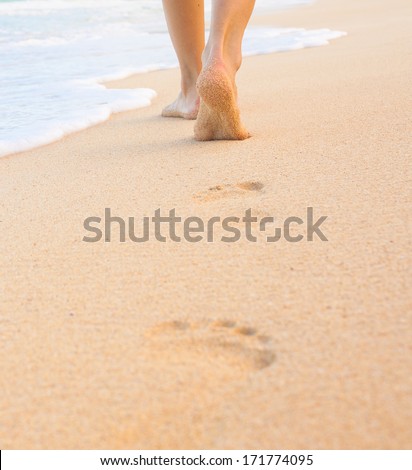 Beach travel. Woman walking on sand beach leaving footprint in the sand.