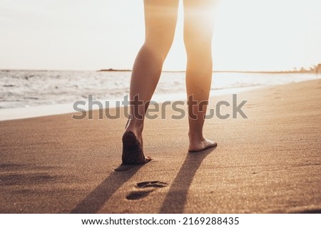 Beach travel - woman walking on sand beach leaving footprints in the sand. Closeup detail of female feet and golden sand on Tenerife beach.