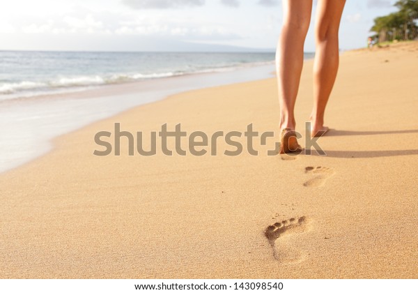 ビーチトラベル – 砂浜を歩く女性が、砂に足跡を残す。カナパリビーチ 