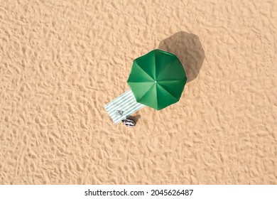 Beach umbrella near towel and other vacationist's stuff on sand, aerial view