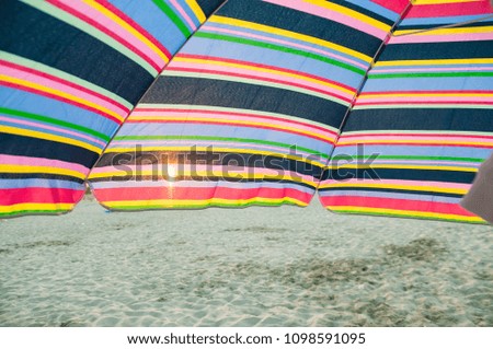 Similar – Colorful striped, closed parasol in close-up on the beach at sunset