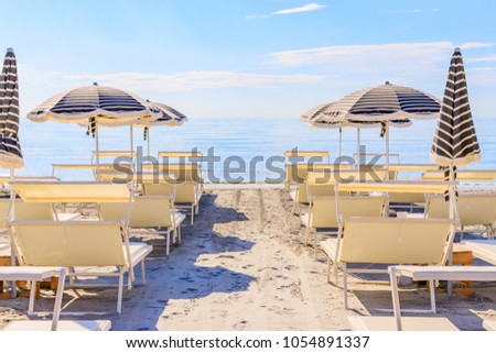 Beach umbrellas and couches on blue sky and sea background on the beach of Italy. Popular Tourist Resort at Adriatic Sea on beach of Milano Marittima, Adriatic coast, Italy
