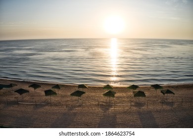 Beach Umbrellas At Sunrise. Sea Current Swims Against The Waves On The Beautiful Sea