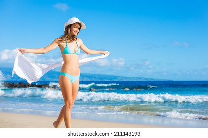 Beach vacation. Beautiful woman in sunhat and bikini enjoying perfect sunny day walking on the beach. Happiness and bliss.