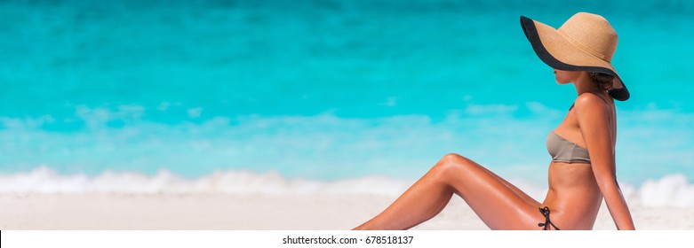 Beach vacation bikini woman relaxing banner with blue water texture copyspace background. Travel holiday panorama concept, girl sunbathing with sun hat lying down on sand. Tropical holidays.