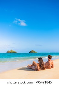 Beach Vacation Couple Relaxing Sunbathing On Hawaiian Tropical Beach In Lanikai, Oahu, Hawaii, USA. American People On Summer Holidays Sun Tanning Lying Down On Sand.