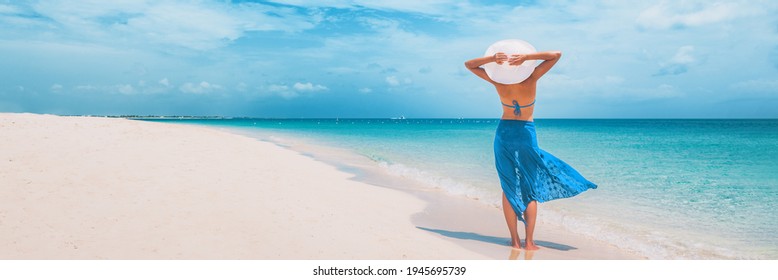 Beach Vacation Happy Woman Walking On Summer Travel Caribbean Holiday With Arms Behind Head Wearing Sun Hat And Sarong Skirt. Ocean Panoramic Banner Background. Elegant Lady Tourist.