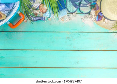 Beach and Vacation Holiday Accessories On Blue Plank. Suitcase for travel, summer women's clothing, sunglasses, accessories and tropical leaves on bright blue background copy space for text top view