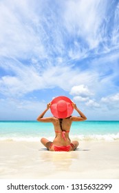 Beach vacation luxury travel cute fashion woman wearing pink swimwear and sun hat relaxing tanning in tropical destination. Girl tourist on summer holiday at vacation resort.