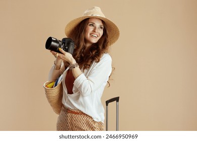 Beach vacation. smiling stylish middle aged housewife in white blouse and shorts isolated on beige background with straw bag, trolley bag, photo camera and summer hat. - Powered by Shutterstock