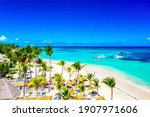 Beach vacation and travel background. Aerial drone view of beautiful atlantic tropical beach with straw umbrellas, palms and boats. Bavaro beach, Punta Cana, Dominican Republic.