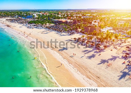 Beach vacation and travel background. Aerial drone view of beautiful atlantic tropical beach with straw umbrellas, palms and boats. Bavaro beach, Punta Cana, Dominican Republic