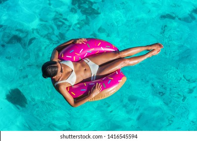 Beach vacation woman relaxing in donut inflatable float floating on ocean in Caribbean travel summer getaway. Girl in white bikini top view.