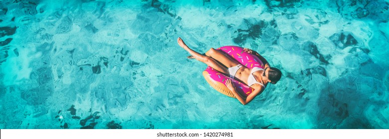 Beach vacation woman relaxing in pool float donut inflatable ring floating on turquoise ocean water background in Caribbean travel summer banner panorama. Girl in white bikini top drone view.