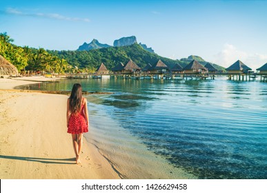 Beach vacation woman walking on Bora Bora island in Tahiti, French Polynesia at sunset with Mount Otemanu and overwater bungalows luxury hotel in the background.