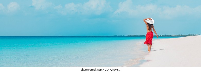 Beach vacation woman walking on summer travel Caribbean holiday wearing white sun hat and sarong skirt. Ocean panoramic banner background. Elegant lady tourist - Powered by Shutterstock