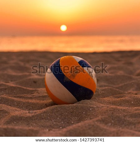 Beach volley ball resting on the sand with a blurred sunset background