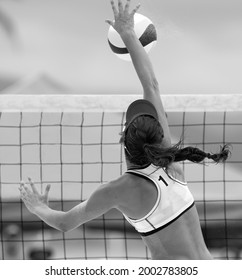 A Beach Volleyball Player Is Jumping At The Net And Spiking The Ball Down In Vertical Black And White Image Format