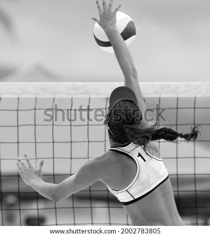 A Beach Volleyball Player Is Jumping At The Net And Spiking The Ball Down In Vertical Black And White Image Format
