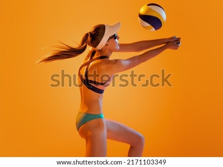 Beach volleyball. Sportive female volleyball player in sport swimsuit training with ball isolated on orange color background. Sport, healthy lifestyle, team, fitness concept. Vacation, summer sports
