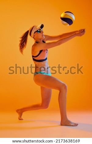 Beach volleyball. Sportive young woman, volleyball player training with ball isolated on orange color background. Sport, healthy lifestyle, team, fitness concept. Vacation, summer sports games