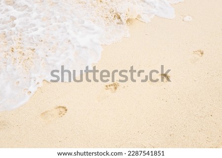 Beach, wave and footprints during the day. Texture background Footprints of human feet on the sand near the water on the beach.