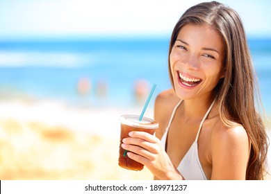 Beach woman drinking cold drink beverage having fun at beach party. Female babe in bikini enjoying Ice tea, coke or alcoholic drink smiling happy laughing looking at camera. Beautiful mixed race girl