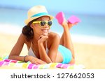 Beach woman funky happy and colorful wearing sunglasses and beach hat having summer fun during travel holidays vacation. Young multiracial trendy cool hipster woman in bikini lying in the sand.