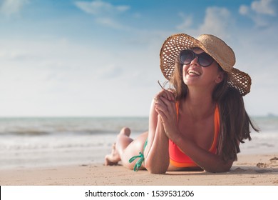 Beach woman funky happy and colorful wearing sunglasses and beach hat having summer fun during travel holidays vacation. Young trendy cool hipster woman in bikini lying in the sand. - Powered by Shutterstock