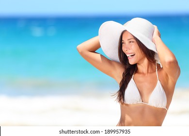 Beach woman happy smiling laughing lifestyle. Bikini girl wearing sun hat looking to side at copy space excited at joyful. Beautiful sexy mixed race woman having fun on summer travel vacation.