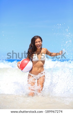 Beach woman playing with ball having fun splashing water laughing happy. Young mixed race asian caucasian woman playing ball in sea waves - smiling, enjoying the sun. Big Island, Hawaii