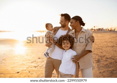 Beachside bonding. Happy multiracial family walking and enjoying time together on beach during holidays. Parents holding and embracing their kids, walking along coastline