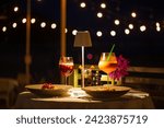 beachside dinner table,Beachside dinner table with one large challah, two bottles of red wine, two wine glasses, two tea lights in jars, one small vase with flowers, at night, with hanging light nearb