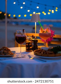 Beachside dinner table,Beachside dinner table with one large challah, two bottles of red wine, two wine glasses, two tea lights in jars, one small vase with flowers, at night, with hanging light nearb