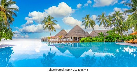 Beachside tourism landscape. Luxurious beach resort poolside, swimming pool and beach chairs or loungers, umbrellas with tropical palm trees and blue sky. Summer travel and vacation background concept - Shutterstock ID 2104948745