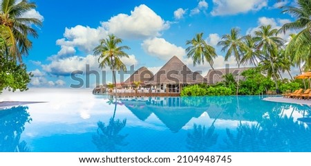 Beachside tourism landscape. Luxurious beach resort poolside, swimming pool and beach chairs or loungers, umbrellas with tropical palm trees and blue sky. Summer travel and vacation background concept